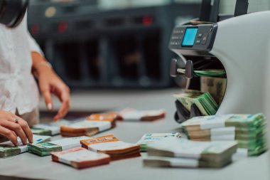 Banka çalışanları banka kasasında kağıt banknotları sıralarken ve sayarken para sayma makinesi kullanıyorlar. Bankada büyük miktarda para var.. 