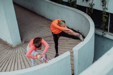 Two women warming up together and preparing for a morning run in an urban environment. Selective focus . 