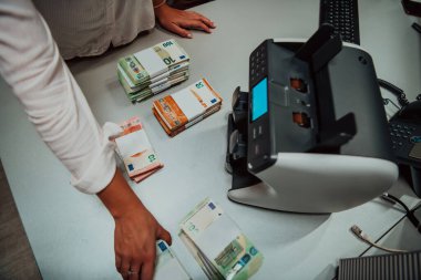 Banka çalışanları banka kasasında kağıt banknotları sıralarken ve sayarken para sayma makinesi kullanıyorlar. Bankada büyük miktarda para var.. 