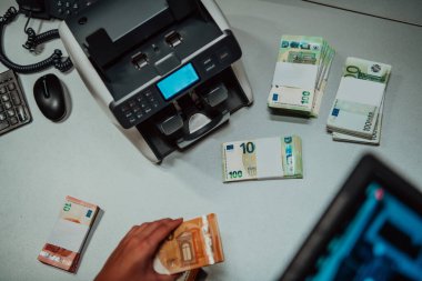 Banka çalışanları banka kasasında kağıt banknotları sıralarken ve sayarken para sayma makinesi kullanıyorlar. Bankada büyük miktarda para var.. 