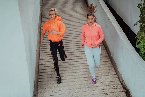 現代の都会の中を走るスポーツウェアを着た2人の女性 スポーティーで健康的なライフスタイルのコンセプト — ストック写真