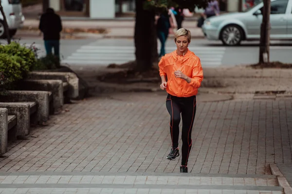 A blonde in a sports outfit is running around the city in an urban environment. The hot blonde maintains a healthy lifestyle