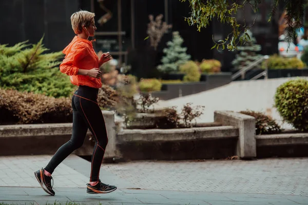 A blonde in a sports outfit is running around the city in an urban environment. The hot blonde maintains a healthy lifestyle