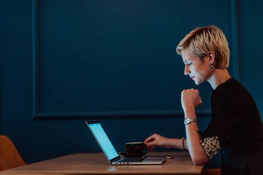 Bir kafede oturan iş kadını bir dizüstü bilgisayar üzerinde çalışmaya ve çevrimiçi toplantılara katılmaya odaklanmış. Seçici odak