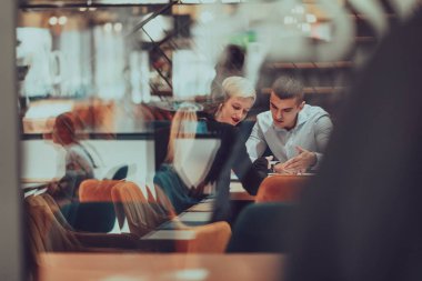 Photo through the glass of a group of business people sitting in a cafe and discussing business plans and ideas for new online commercial services. 