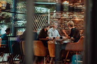 Photo through the glass of a group of business people sitting in a cafe and discussing business plans and ideas for new online commercial services. 