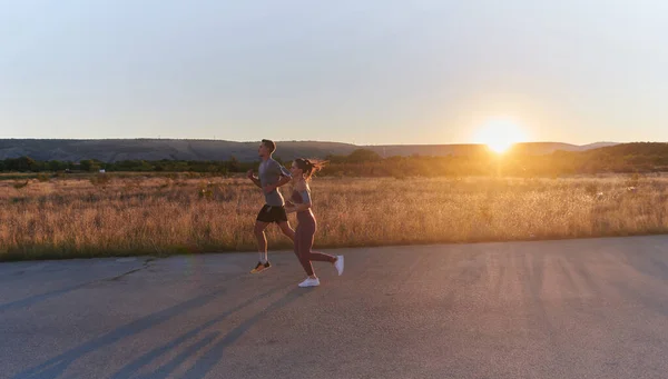 朝の早い時間に一緒に走るハンサムな若いカップルは 魅惑的な日の出が暖かい輝きを放ち 彼らの共有愛と活力を象徴しています — ストック写真