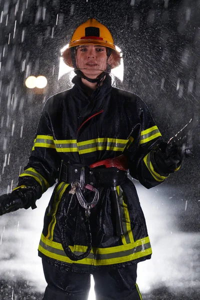 勇敢な救助任務で危険な雨の夜を通ってプロの制服を着た決定的な女性消防士は 彼女の絶え間ない勇気と命を救うというコミットメントを示しています — ストック写真