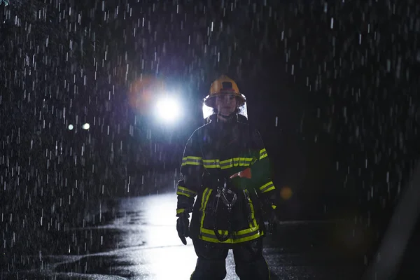 一名身穿职业制服的坚定的女消防员在险象环生的雨夜中大步走过 勇敢地执行营救任务 表现出她坚定不移的勇气和拯救生命的决心 — 图库照片