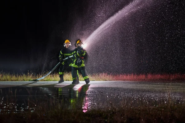 消防员使用水龙带以消除火警危险 执行危险救援任务的男女消防员小组 — 图库照片
