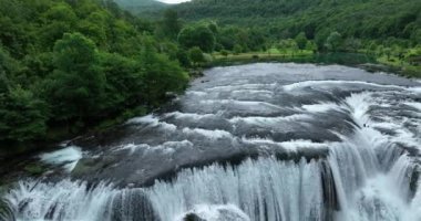 Bosna-Hersek 'te büyük bir şelaleyle vahşi nehrin destansı görüntüsünü oluşturan şaşırtıcı yavaş çekim. Kristal berrak içme suyu güzel şelale bulutlu yaz gününde.