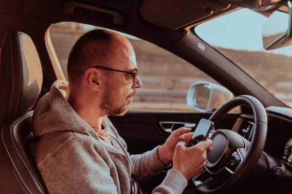 Mężczyzna Okularach Przeciwsłonecznych Prowadzący Samochód Wpisujący Wiadomość Smartfonie Zachodzie Słońca — Zdjęcie stockowe