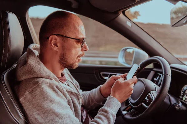 Mężczyzna Okularach Przeciwsłonecznych Prowadzący Samochód Wpisujący Wiadomość Smartfonie Zachodzie Słońca — Zdjęcie stockowe