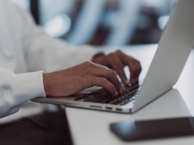 Modern ofis ortamında, Afrikalı Amerikalı bir işadamı özenle dizüstü bilgisayarı üzerinde çalışıyor, profesyonel çevresindeki kararlılığı, hırsı ve verimliliği somutlaştırıyor.. 