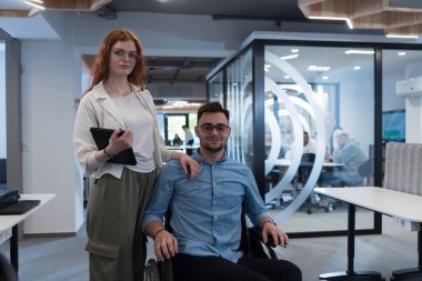 Genç iş arkadaşları, işbirlikçi iş arkadaşları, aralarında tekerlekli sandalyedeki bir kişinin de bulunduğu, modern cam ofis koridorunun yanından geçerek, çeşitliliği, takım çalışmasını ve güçlendirmeyi resmediyorlar.