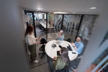 Bir grup genç girişimci odaklanmış bir toplantıya katılıyor, çeşitli iş stratejilerini tartışıyor ve işbirliği içinde zorlu sorunları çözüyorlar, hırslarını, yaratıcılıklarını ve