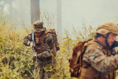 Bir grup modern savaş askeri tehlikeli uzak orman bölgelerinde savaşıyor. Bir grup asker modern silahlarla düşman hattında savaşıyor. Savaş ve askerlik kavramı.