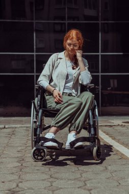 Modern bir şirket binasının önünde, tekerlekli sandalyede kendinden emin bir şekilde oturan genç bir kadın, güçlendirmeyi, kapsayıcılığı ve iş dünyasındaki zorlukların üstesinden gelme gücünü simgeliyor.. 