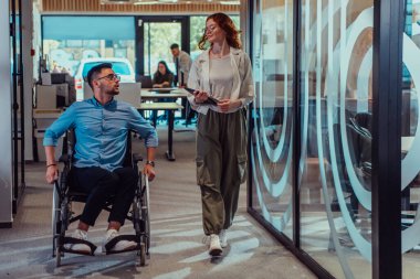 Genç iş arkadaşları, işbirlikçi iş arkadaşları, aralarında tekerlekli sandalyedeki bir kişinin de bulunduğu, modern cam ofis koridorunun yanından geçerek, çeşitliliği, takım çalışmasını ve güçlendirmeyi resmediyorlar.