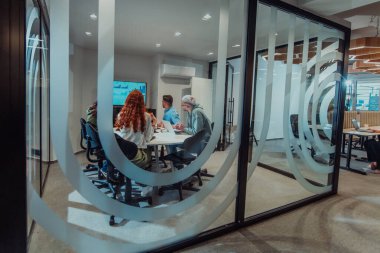 Bir grup genç girişimci odaklanmış bir toplantıya katılıyor, çeşitli iş stratejilerini tartışıyor ve işbirliği içinde zorlu sorunları çözüyorlar, hırslarını, yaratıcılıklarını ve