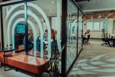 Bir grup genç girişimci odaklanmış bir toplantıya katılıyor, çeşitli iş stratejilerini tartışıyor ve işbirliği içinde zorlu sorunları çözüyorlar, hırslarını, yaratıcılıklarını ve