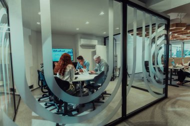 Bir grup genç girişimci odaklanmış bir toplantıya katılıyor, çeşitli iş stratejilerini tartışıyor ve işbirliği içinde zorlu sorunları çözüyorlar, hırslarını, yaratıcılıklarını ve