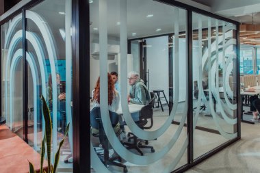 Bir grup genç girişimci odaklanmış bir toplantıya katılıyor, çeşitli iş stratejilerini tartışıyor ve işbirliği içinde zorlu sorunları çözüyorlar, hırslarını, yaratıcılıklarını ve