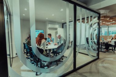 Bir grup genç girişimci odaklanmış bir toplantıya katılıyor, çeşitli iş stratejilerini tartışıyor ve işbirliği içinde zorlu sorunları çözüyorlar, hırslarını, yaratıcılıklarını ve