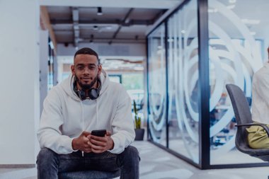 Akıllı telefon kullanırken kulaklık takan Afrikalı Amerikalı işadamı, modern bir ofiste tamamen işine odaklanmış, verimlilik ve çağdaş profesyonelliği sergiliyor.. 