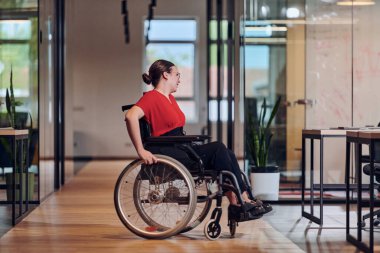 Tekerlekli sandalyedeki modern genç bir iş kadını cam duvarlı ofisleri olan, iş dünyasındaki azim ve yenilikleri somutlaştıran, kapsamlı bir çalışma alanıyla çevrilidir.. 