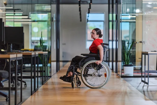 一个坐在轮椅上的现代女商人被一个有玻璃墙办公室的包容性工作空间所围绕 体现了商界的决心和创新精神 — 图库照片