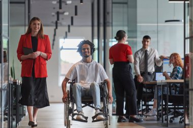 Modern cam duvarlı bir ofiste çalışan bir grup genç iş adamı çeşitliliğin ve işbirliğinin özünü yakalar, aralarında tekerlekli sandalyedeki Afrikalı Amerikalı bir işadamının da bulunduğu iki meslektaşı