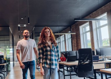 Genç bir Afrikalı Amerikalı işadamı ve turuncu saçlı modern bir iş kadını kollarını kavuşturmuş, çağdaş ofis ortamında güven ve birlik saçan, dinamiği simgeleyen