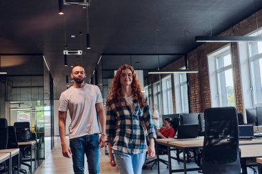 Genç bir Afrikalı Amerikalı işadamı ve turuncu saçlı modern bir iş kadını kollarını kavuşturmuş, çağdaş ofis ortamında güven ve birlik saçan, dinamiği simgeleyen