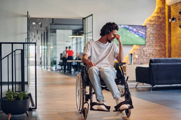 A sad businessman in a wheelchair occupies a hallway within a modern startup coworking center, embodying inclusivity and determination in the business environment.