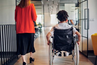 Modern cam duvarlı bir ofiste çalışan bir grup genç iş adamı çeşitliliğin ve işbirliğinin özünü yakalar, aralarında tekerlekli sandalyedeki Afrikalı Amerikalı bir işadamının da bulunduğu iki meslektaşı