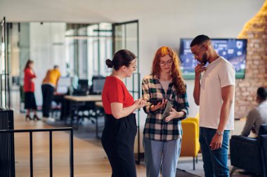 Turuncu saçlı bir kız ve Afro-Amerikan bir adam da dahil olmak üzere bir grup genç iş adamı modern bir şirket koridorunda duruyor ve akıllı telefondaki iş ilerlemesini birlikte inceliyorlar.