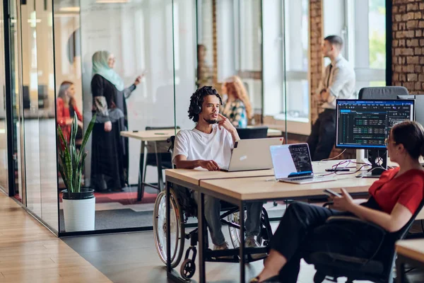 一个年轻的商业团体 包括坐在轮椅上的非洲裔美国商人 在一个现代玻璃办公室里合作 积极参与电脑和笔记本电脑的研发 共同解决这个问题 — 图库照片