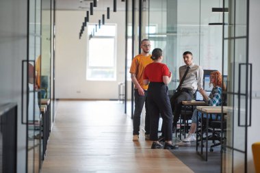 Tekerlekli sandalyedeki Afrikalı Amerikalı bir işadamı da dahil olmak üzere bir iş grubu, modern bir cam ofis içinde, bilgisayar ve dizüstü bilgisayarın etrafında aktif olarak iş birliği yaparak çeşitli çözümler üretiyor.