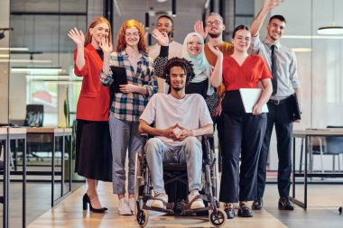 Genç iş adamlarından oluşan çeşitli bir grup, modern bir girişim olan cam kaplı bir ofiste, tekerlekli sandalyedeki bir kişi, bir Afrikalı Amerikalı genç adam ve bir tesettür ile bir araya geliyor.