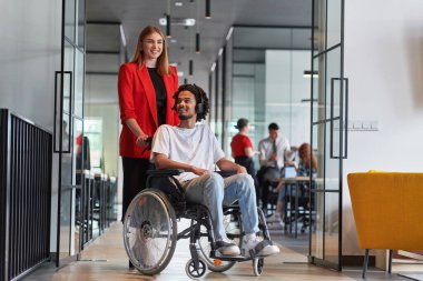 Modern cam duvarlı bir ofiste çalışan bir grup genç iş adamı çeşitliliğin ve işbirliğinin özünü yakalar, aralarında tekerlekli sandalyedeki Afrikalı Amerikalı bir işadamının da bulunduğu iki meslektaşı