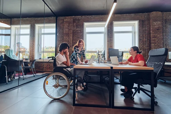 一个年轻的商业团体 包括坐在轮椅上的非洲裔美国商人 在一个现代玻璃办公室里合作 积极参与电脑和笔记本电脑的研发 共同解决这个问题 — 图库照片