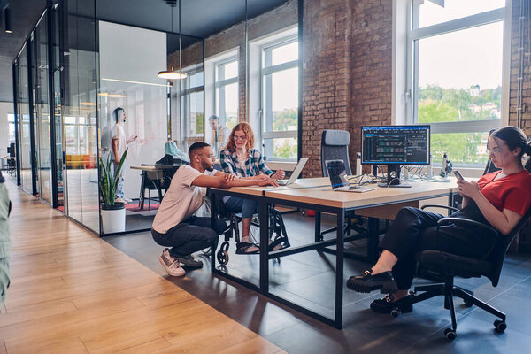 Разнообразная группа бизнес-профессионалов сотрудничает в современном стартап-центре, используя смесь бумажных и технологических инструментов, таких как мобильные телефоны и компьютеры, чтобы коллективно