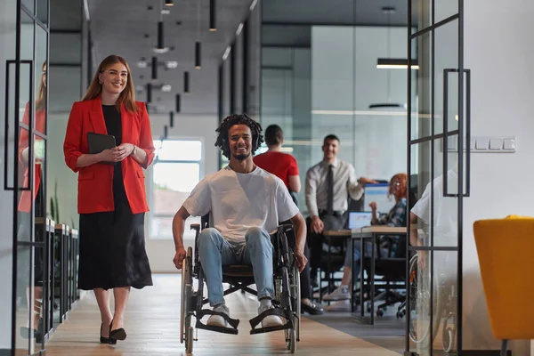 近代的なガラス張りのオフィスにいる若いビジネスマンのグループは 多様性とコラボレーションの本質を捉え 車椅子にいるアフリカ系アメリカ人のビジネスマンを含む2人の同僚がいます — ストック写真