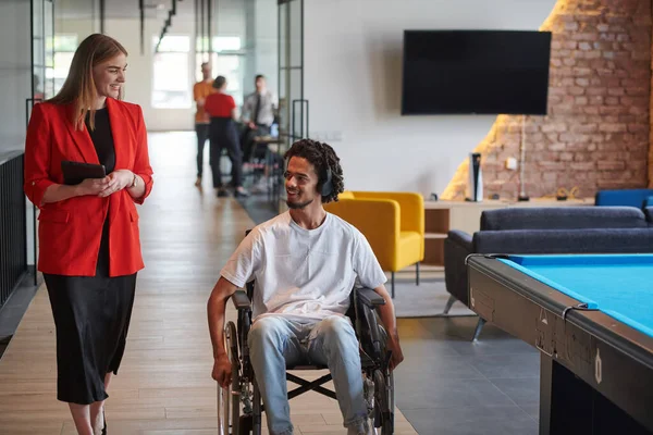 Stock image A group of young business people in a modern glass-walled office captures the essence of diversity and collaboration, while two colleagues, including an African American businessman in a wheelchair