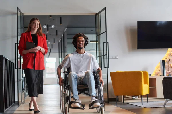 stock image A group of young business people in a modern glass-walled office captures the essence of diversity and collaboration, while two colleagues, including an African American businessman in a wheelchair