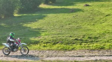 Motokros binicisinin tozlu ve tozlu bir kır yolunda hızlı sürerken ve güzel doğayı keşfederken insansız hava aracı tarafından kovalanırken çekilmiş bir fotoğrafı. Yüksek kalite sinematik yavaş çekim görüntüleri.