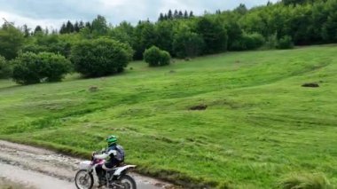 Motokros binicisinin tozlu ve tozlu bir kır yolunda hızlı sürerken ve güzel doğayı keşfederken insansız hava aracı tarafından kovalanırken çekilmiş bir fotoğrafı. Yüksek kalite sinematik yavaş çekim görüntüleri.