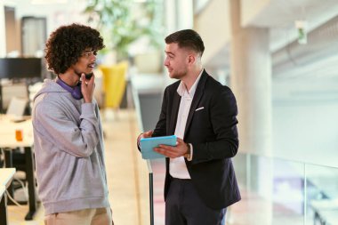 Modern bir ofis ortamında, Afrikalı bir Amerikalı işadamı, yönetmeniyle bir tartışmaya girer, ticari sorunları çözmek için bir tablet kullanır, işbirliği ve teknolojiyi sembolize eder.