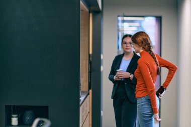 Çağdaş ve geniş ofis ortamının ortasında, iki modern genç kadın bir iş molası sırasında gevşeme ve dinamik işbirliğinin önemini yansıtan bir sohbete girişiyor.